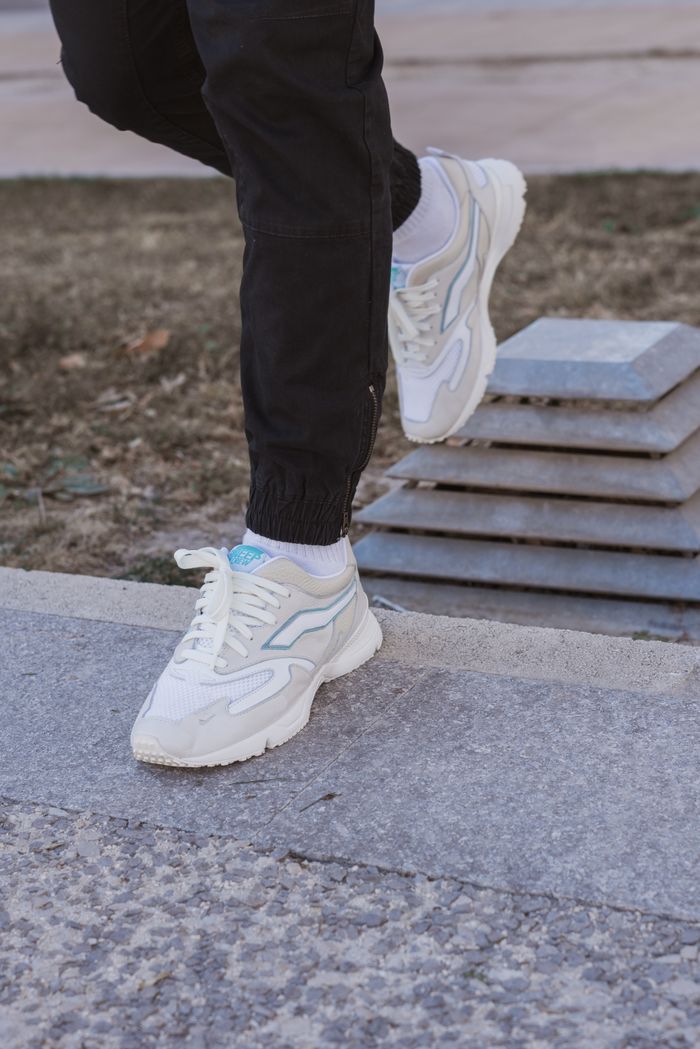 Trendy white sneakers paired with black pants on urban pavement, showcasing fashion-forward style.