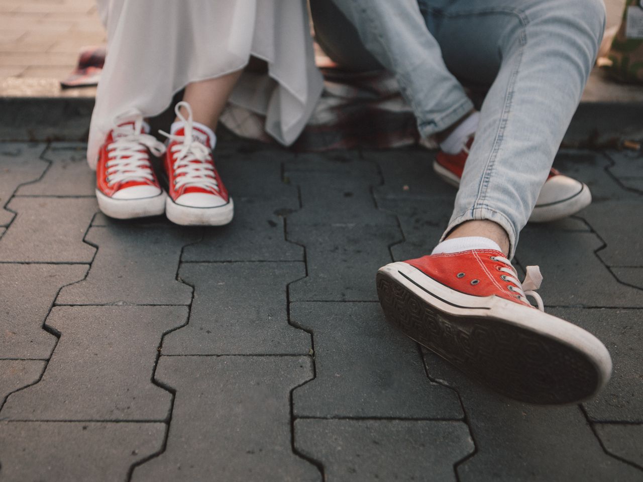 Two people wearing red sneakers sitting on urban pavement, showcasing casual and comfortable style.